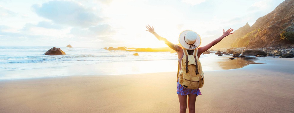 Happy female traveller with backpack and hands up enjoying sunset on the beach